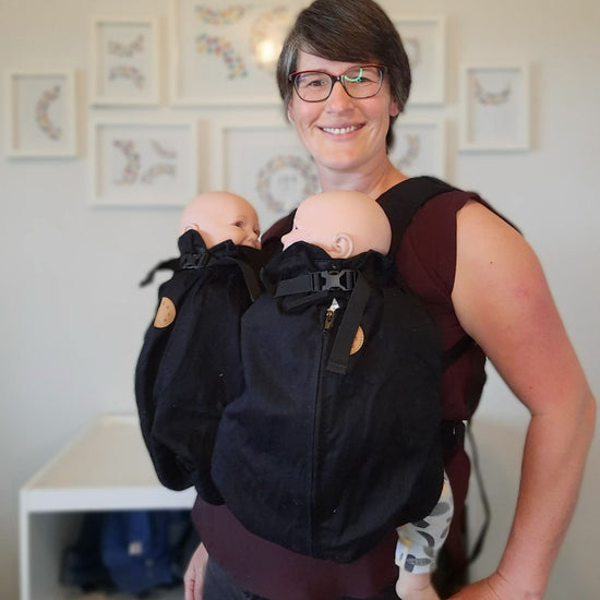 Auckland babywearing consultant wearing twin demo dolls in a black Weego baby carrier