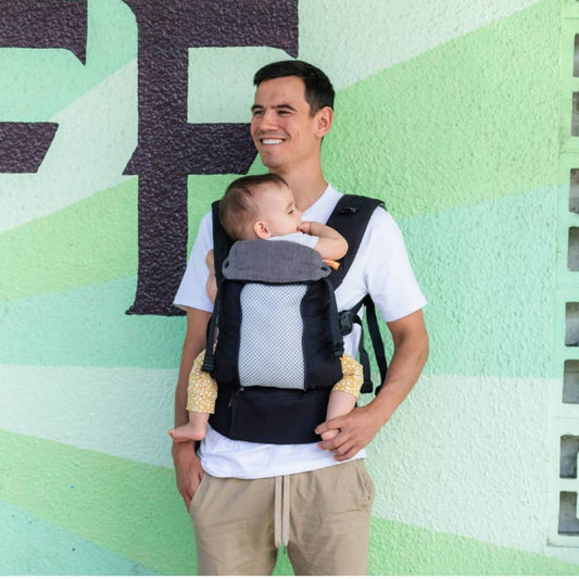 Man carrying infant in a black Beco8 baby carrier.  The mesh panel is open