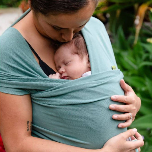 Woman wearing a blue lagoon coloured Boba Serenity stretchy wrap, kissing her childs head