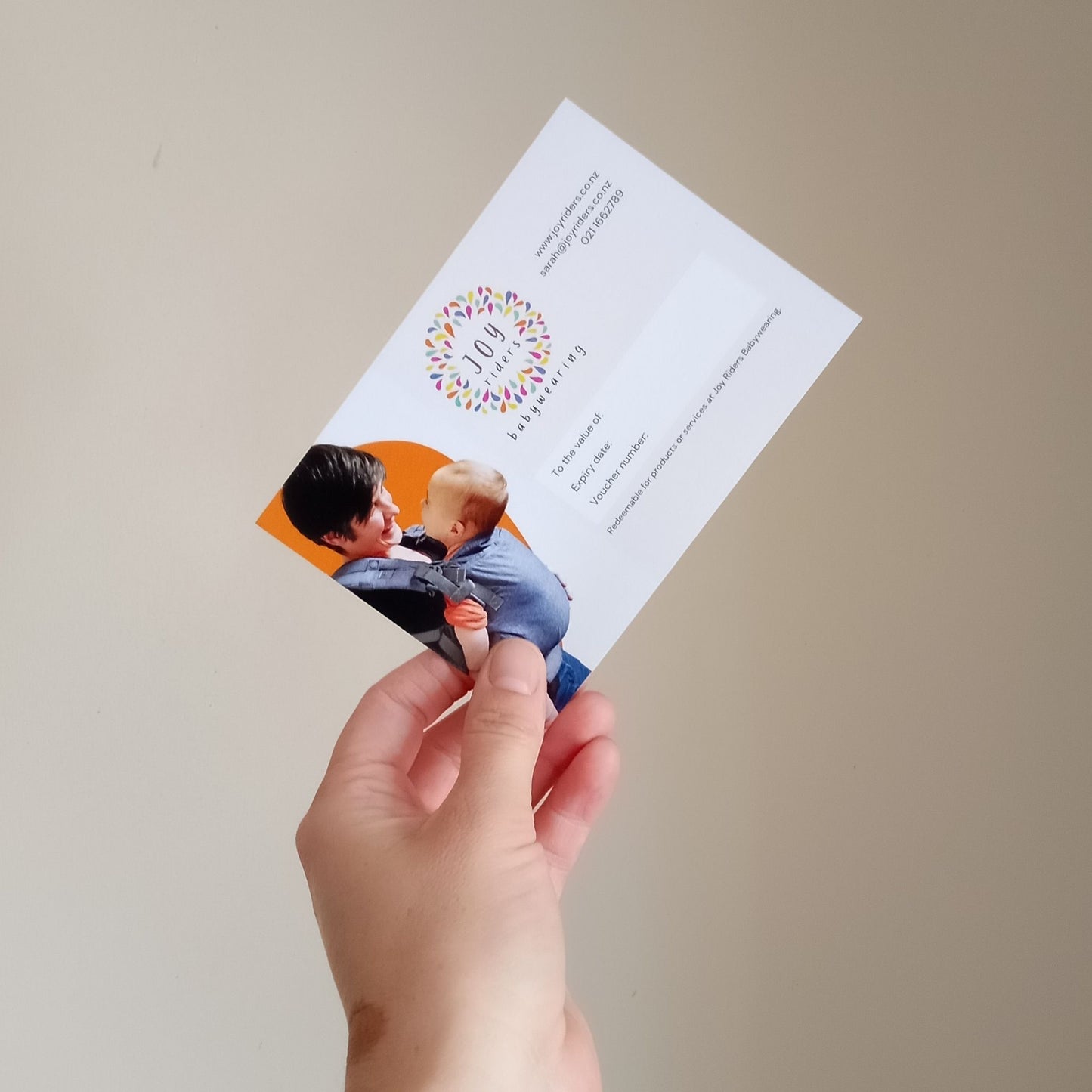 A hand holding a Joy Riders babywearing gift card. redeemable for babywearing consultations or baby carriers