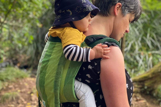 Toddler being carried in green onbuhimo with native bush in background