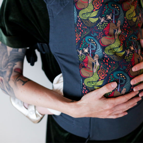 Close up of a man wearing an infant in a Boba $GS with mermaid and unicorn print